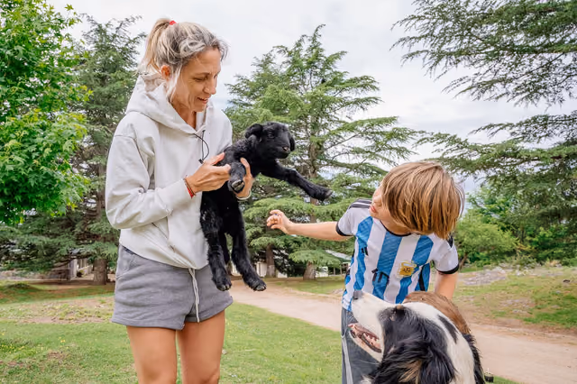Una mujer y un nene alzando un cabrito, con un perro al lado